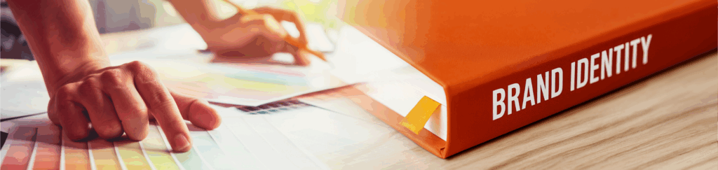 Rarebit Media Blog Banner - Orange book cover with white font labelling "Brand Identity" visually blending into the right side where a pair of hands selects a colour from a colourful plate card.